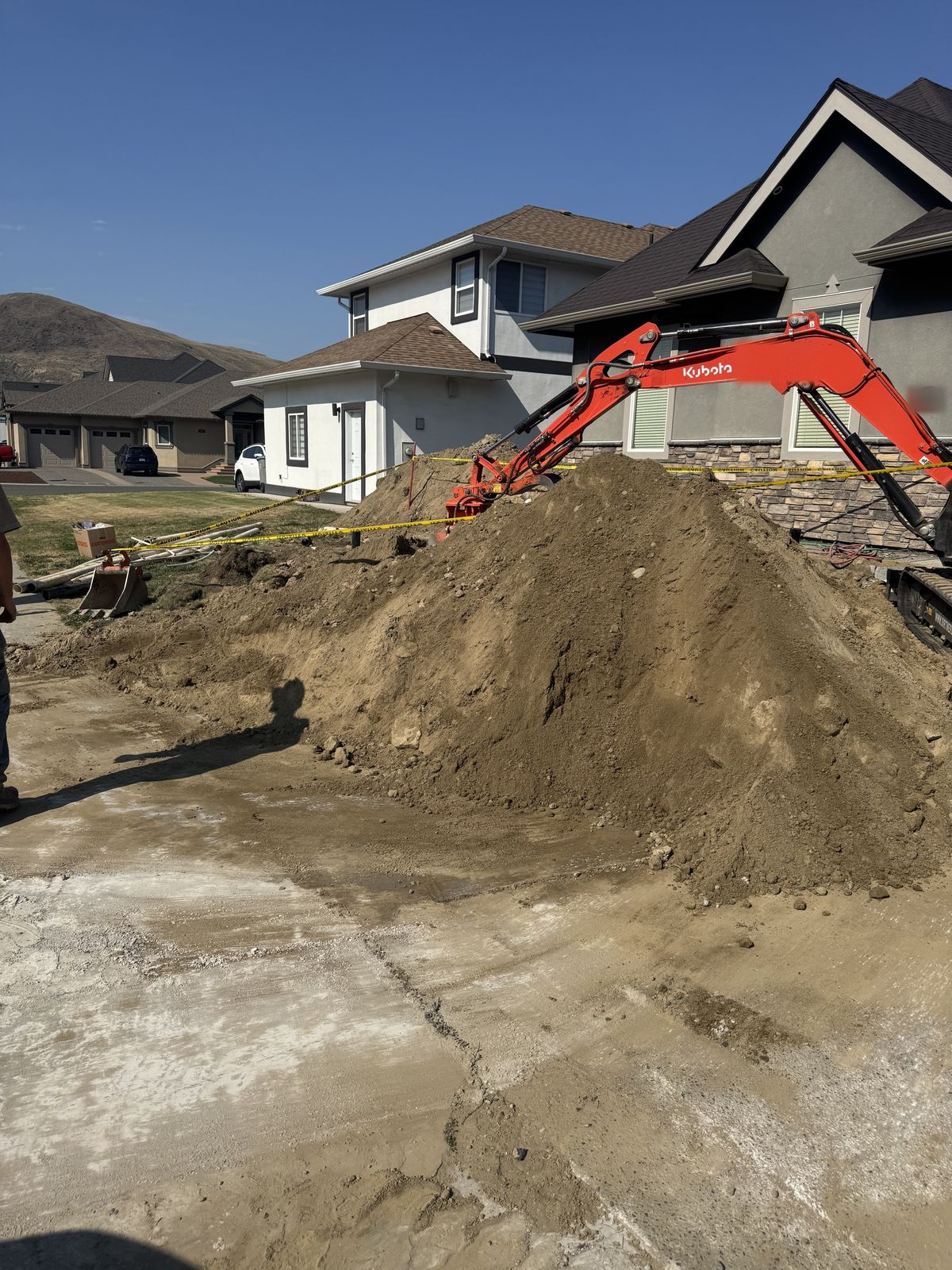 Excavator stockpiling soil on a residential driveway job